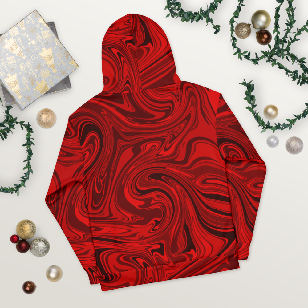 A black and red abstract swirl patterned hoodie laid flat on a light wooden surface. The design features bold, fluid lines creating a modern, artistic effects across the entire hoodie.  The image shows the back view, highlighting the hood and seamless all-over print. Festive ornaments and greenery are placed around the hoodie for decorative holiday-inspired styling. 