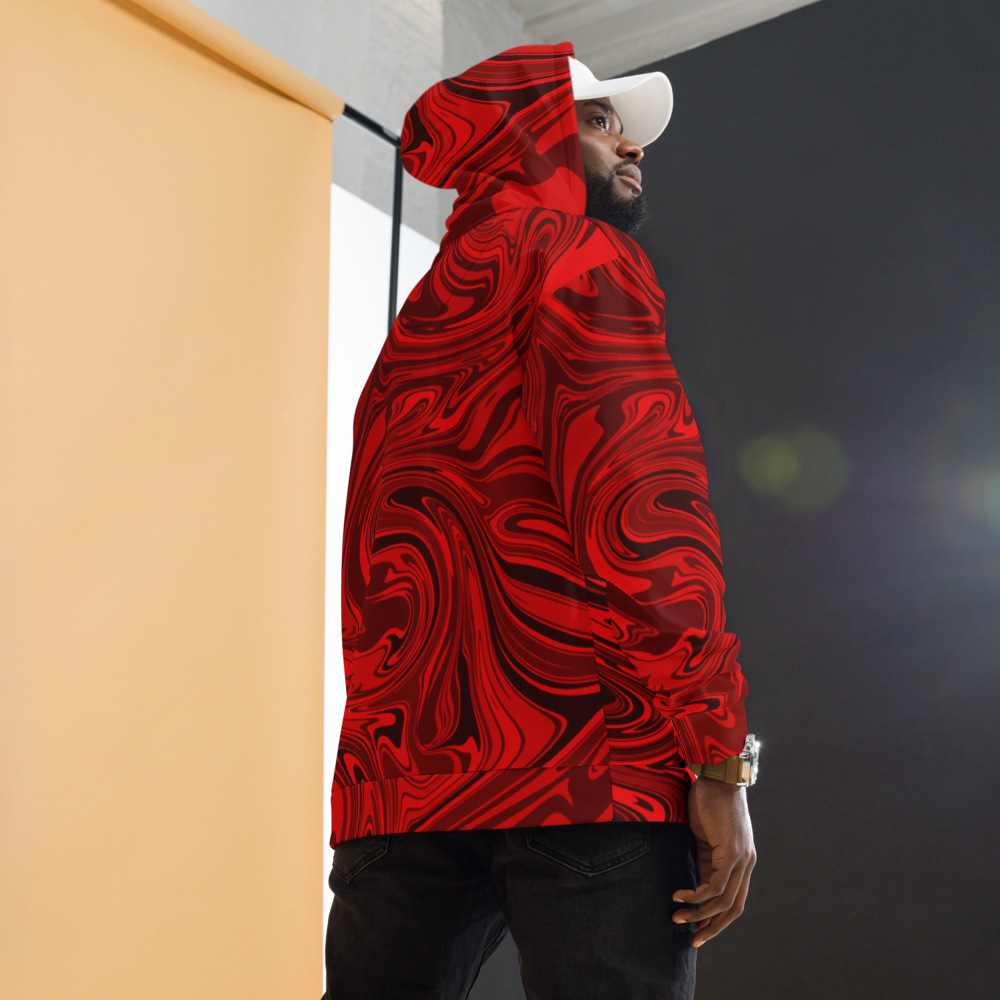 A man wearing a red and black abstract swirl patterned hoodie with a relaxed fit. The design features bold, fluid lines that create a modern, artistic look. The photo shows the back and side view of the hoodie, highlighting its vibrant all-over print and hood detail. He is also wearing dark pants and a white cap against a softly lit studio background. 