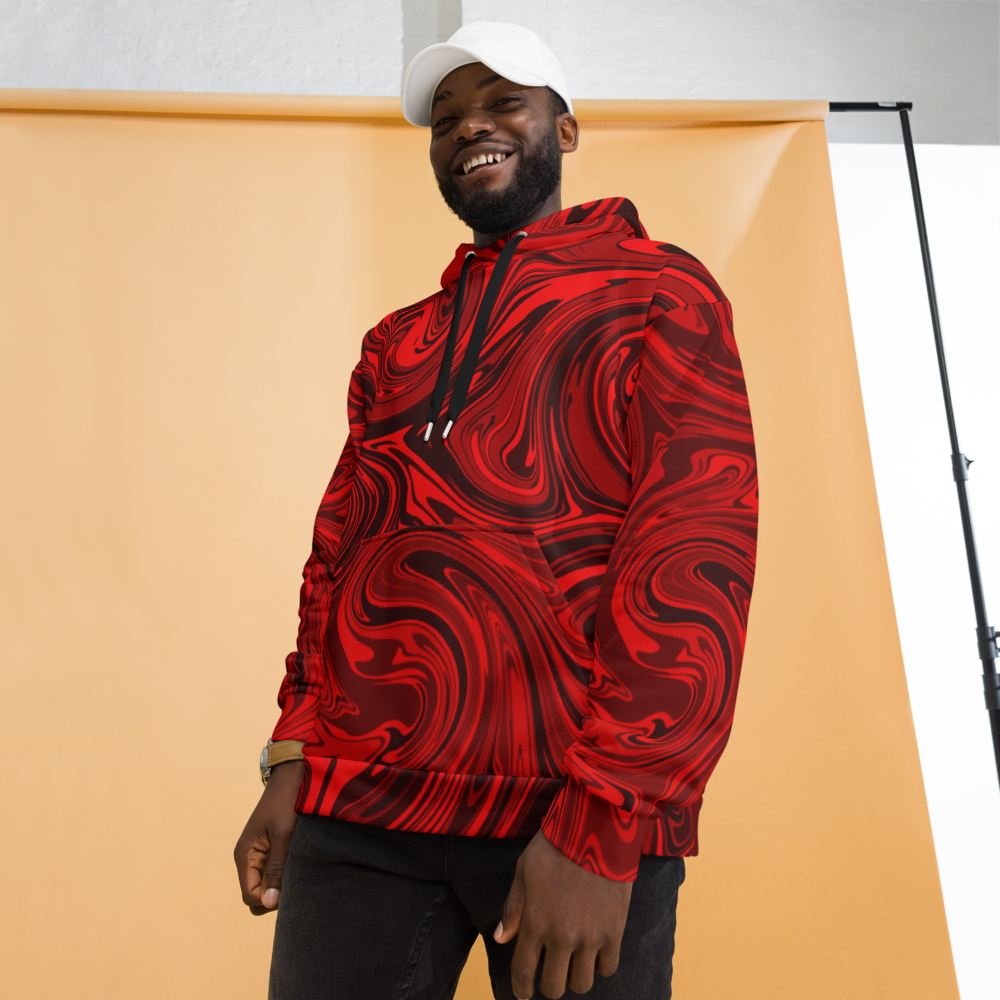 A man smiling while wearing a vibrant red and black abstract swirl patterned hoodie. The hoodie features a relaxed fit with a front pocket and black drawstrings.  The bold, fluid design creates a dynamic, artistic look. He is posing in front of a peach-colored studio backdrop while wearing a white cap and dark pants. 